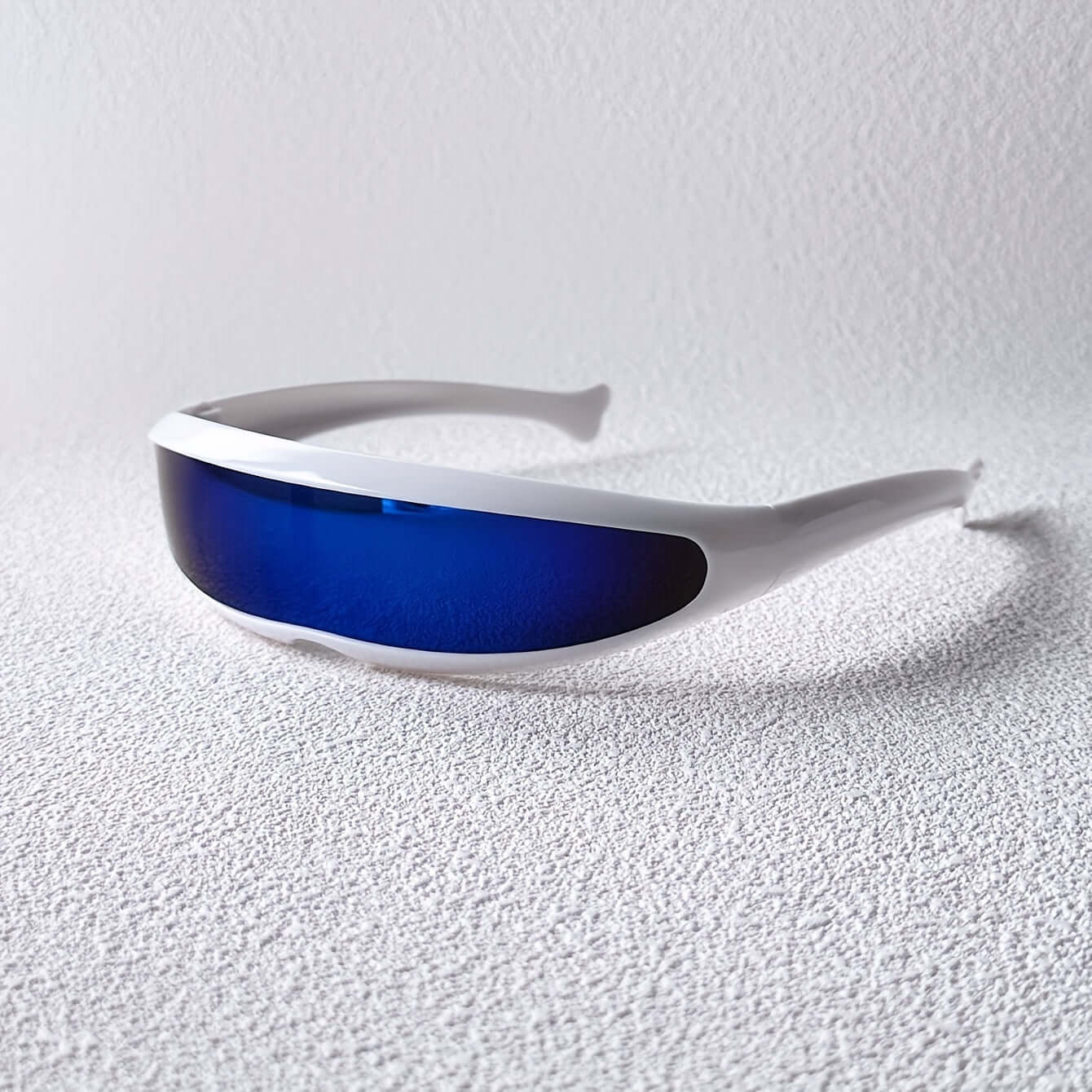 Futuristic fish-shaped sunglasses with blue anti-reflective lenses on a textured surface.