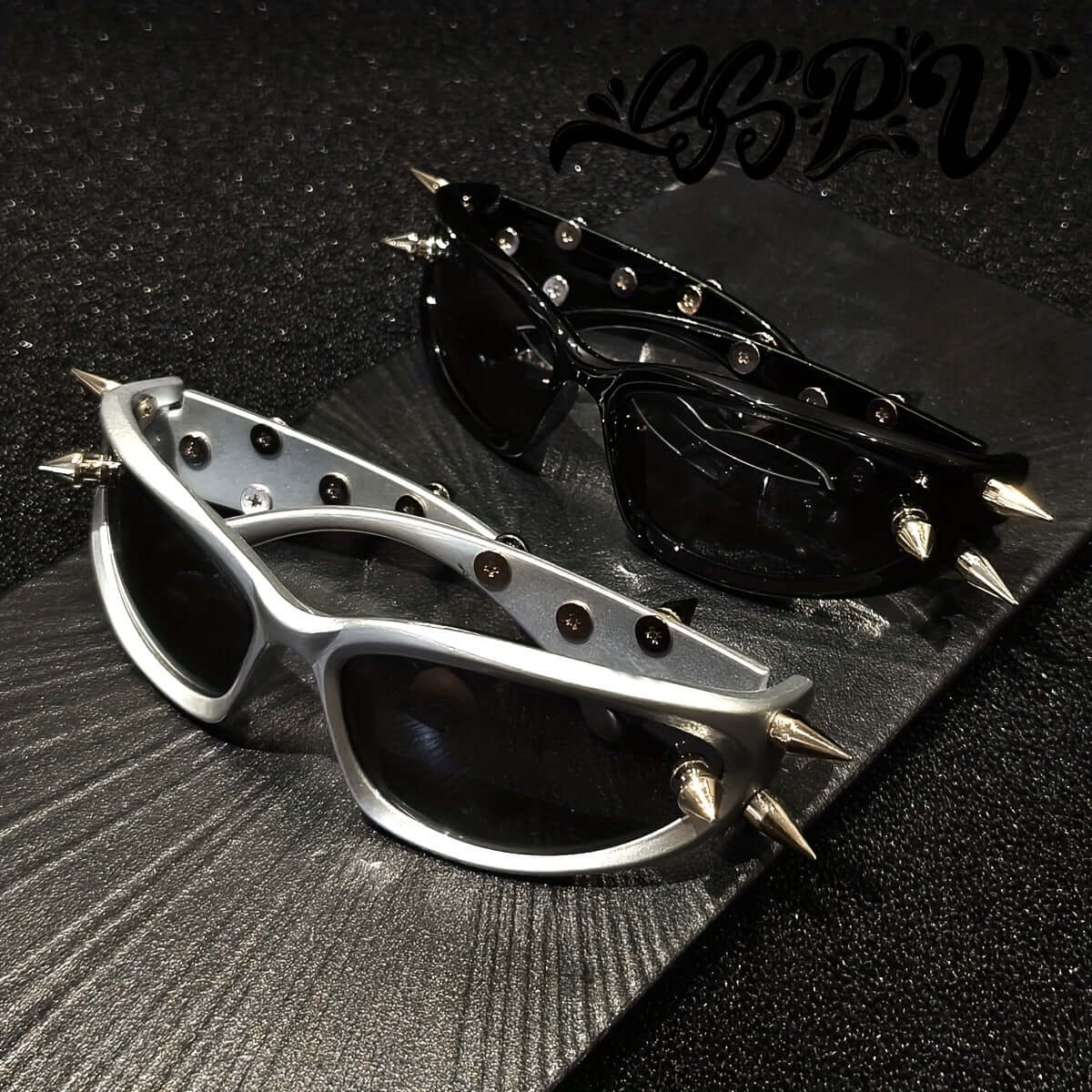 Cyberpunk cat-eye glasses with metal rivet accents, showcasing black and silver designs on a textured black surface.