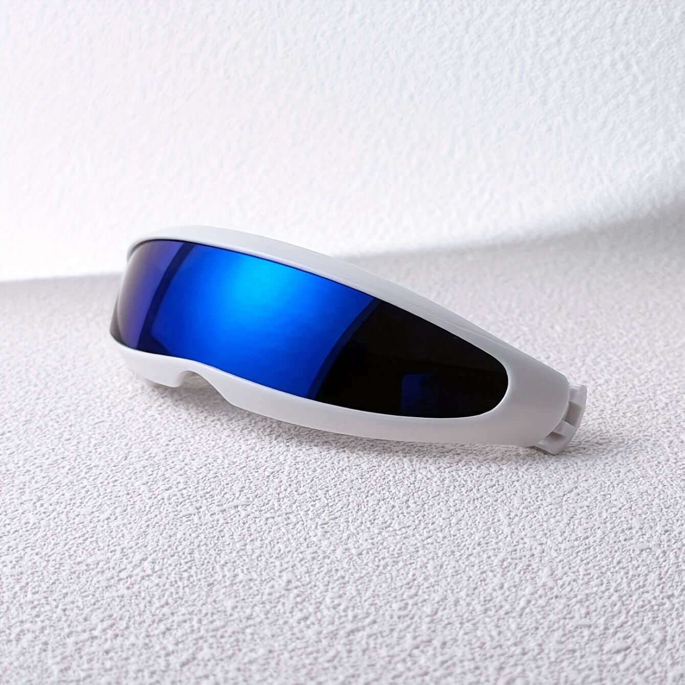 Blue futuristic fish-shaped sunglasses with sleek design and anti-reflective lenses on a textured surface.