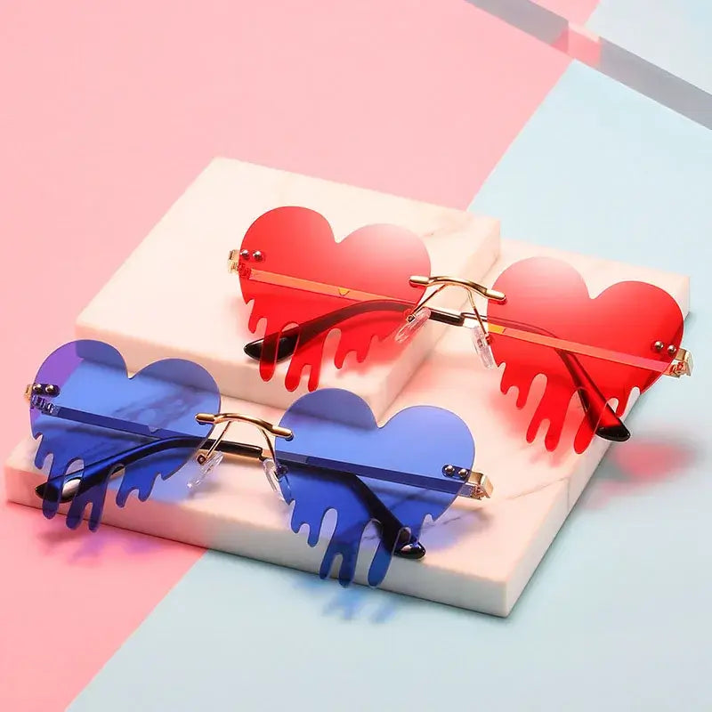 Heart rimless tear-shaped sunglasses in red and blue, unique steampunk style with UV400 protection, displayed on white platforms.