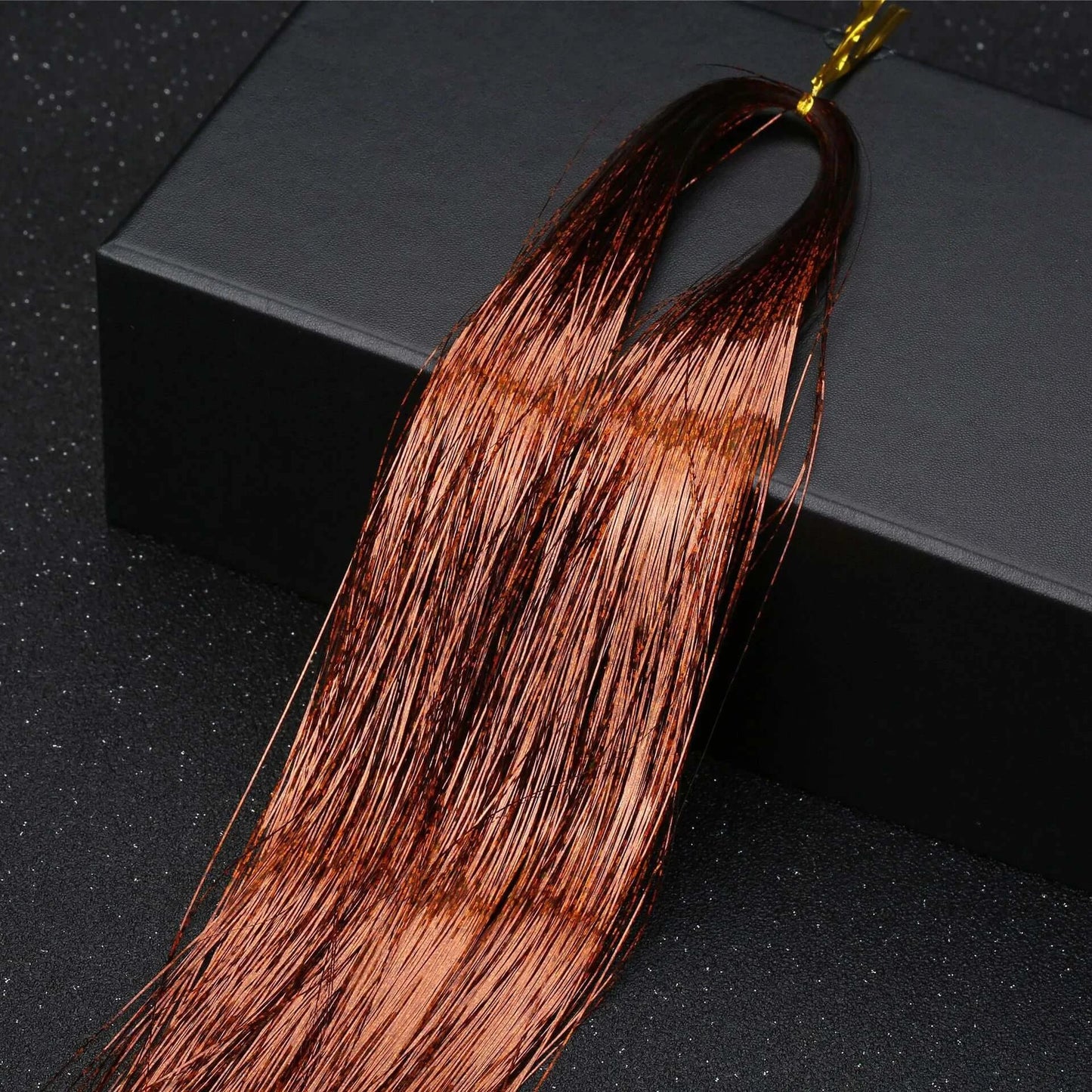 Shiny gold hair tinsel extensions displayed on a black box, perfect for adding sparkle to party hairstyles.