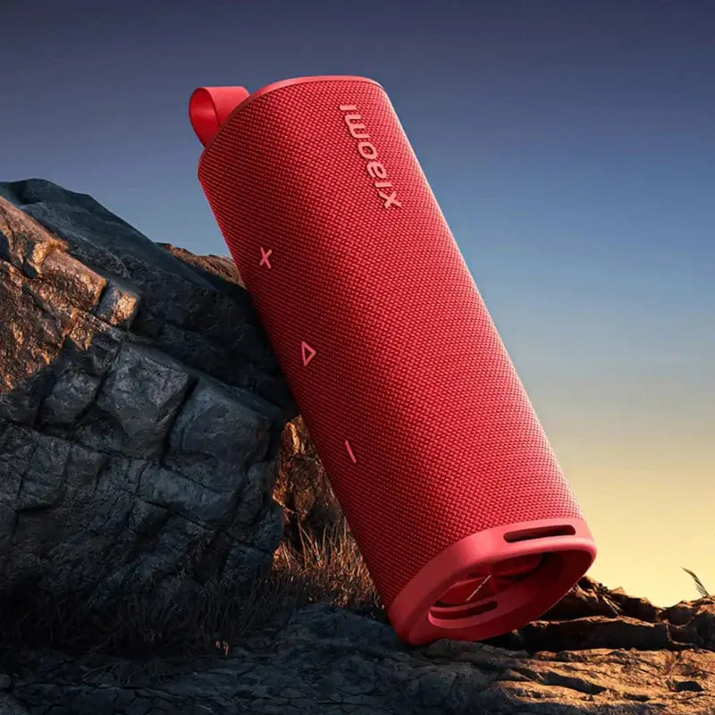 Xiaomi Sound Outdoor 30W Portable Bluetooth Speaker on rocks at sunset, featuring durable design and bright red color.