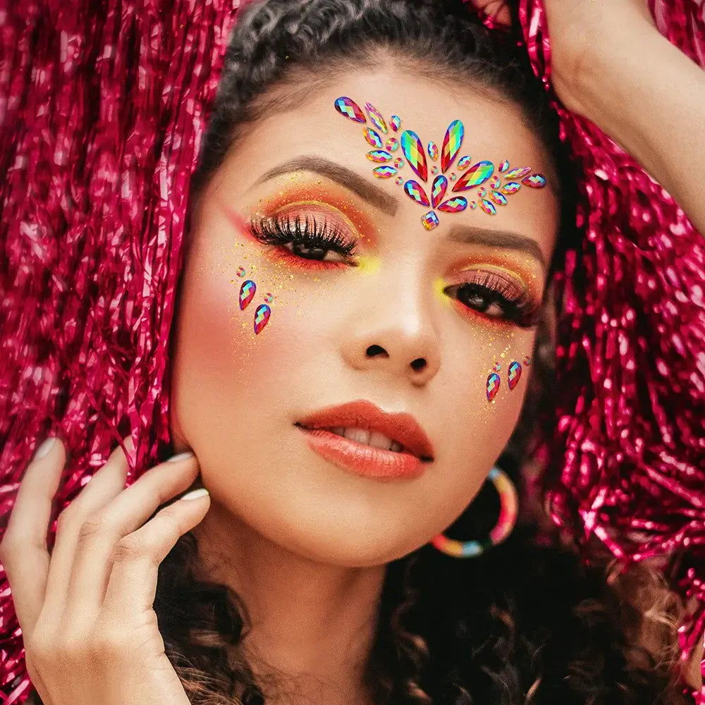 Woman wearing colorful mermaid face jewels for a festival look, featuring sparkling crystal stickers and vibrant makeup against a pink backdrop.