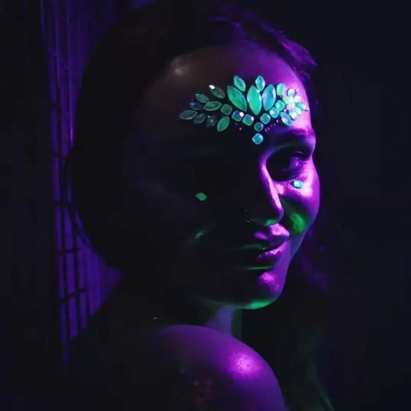 Woman wearing 3D glowing rhinestone face stickers under UV light for a festival look.