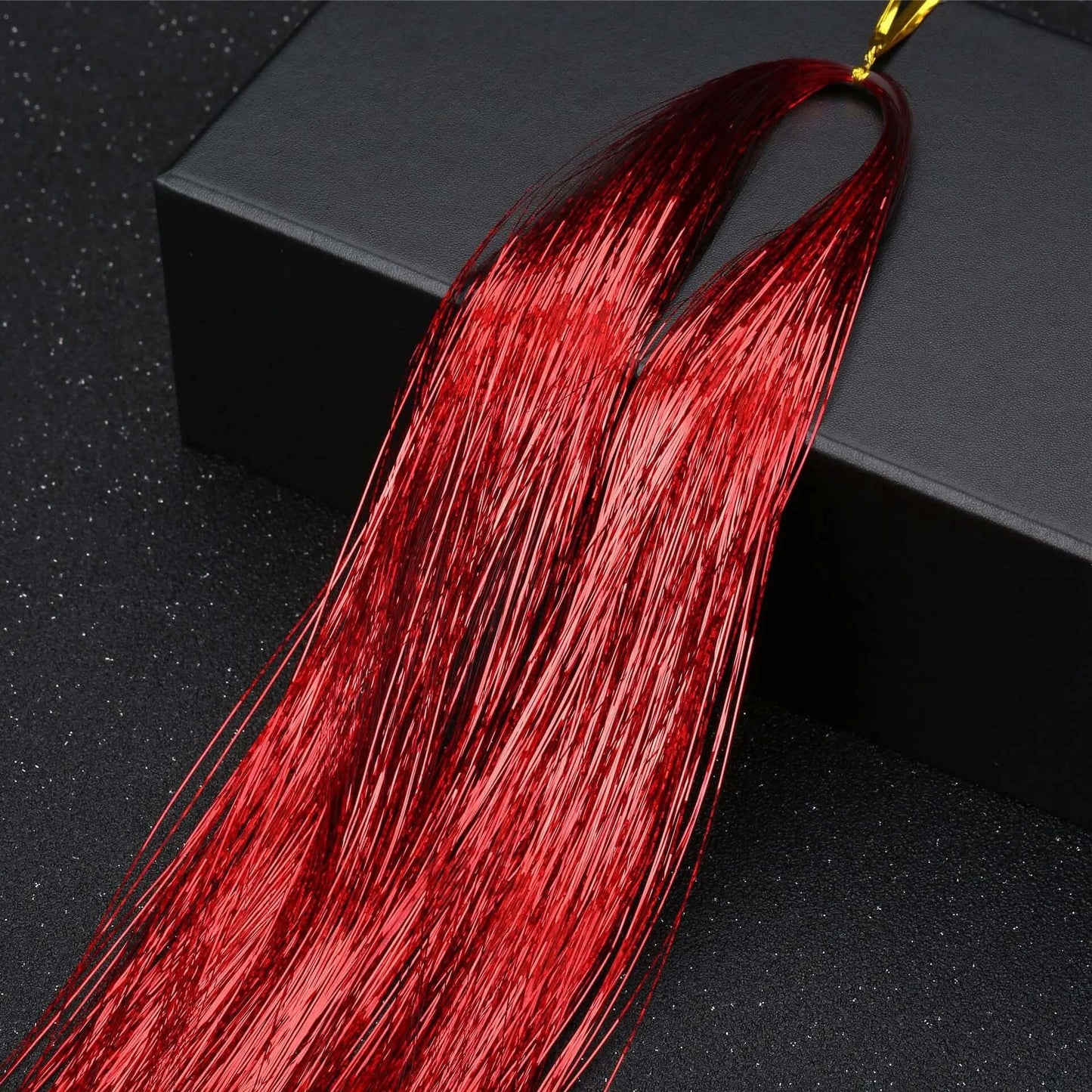 Sparkling red glitter hair tinsel extension displayed on a black background, perfect for parties and festival hairstyles.