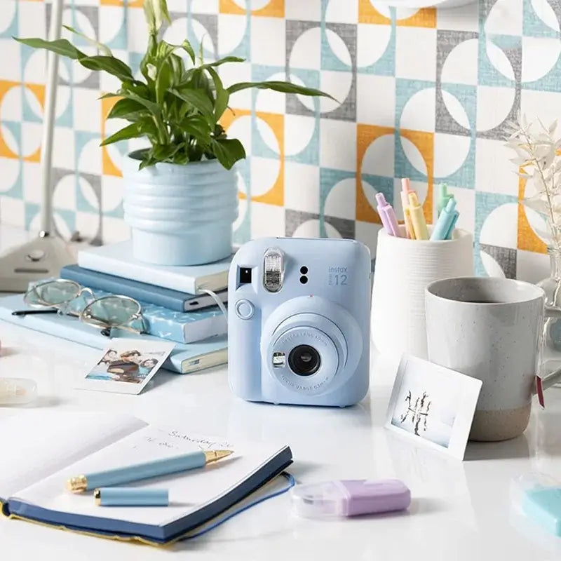 Pastel Blue Fujifilm Instax Mini 12 Instant Camera on desk, surrounded by stationery and decor.