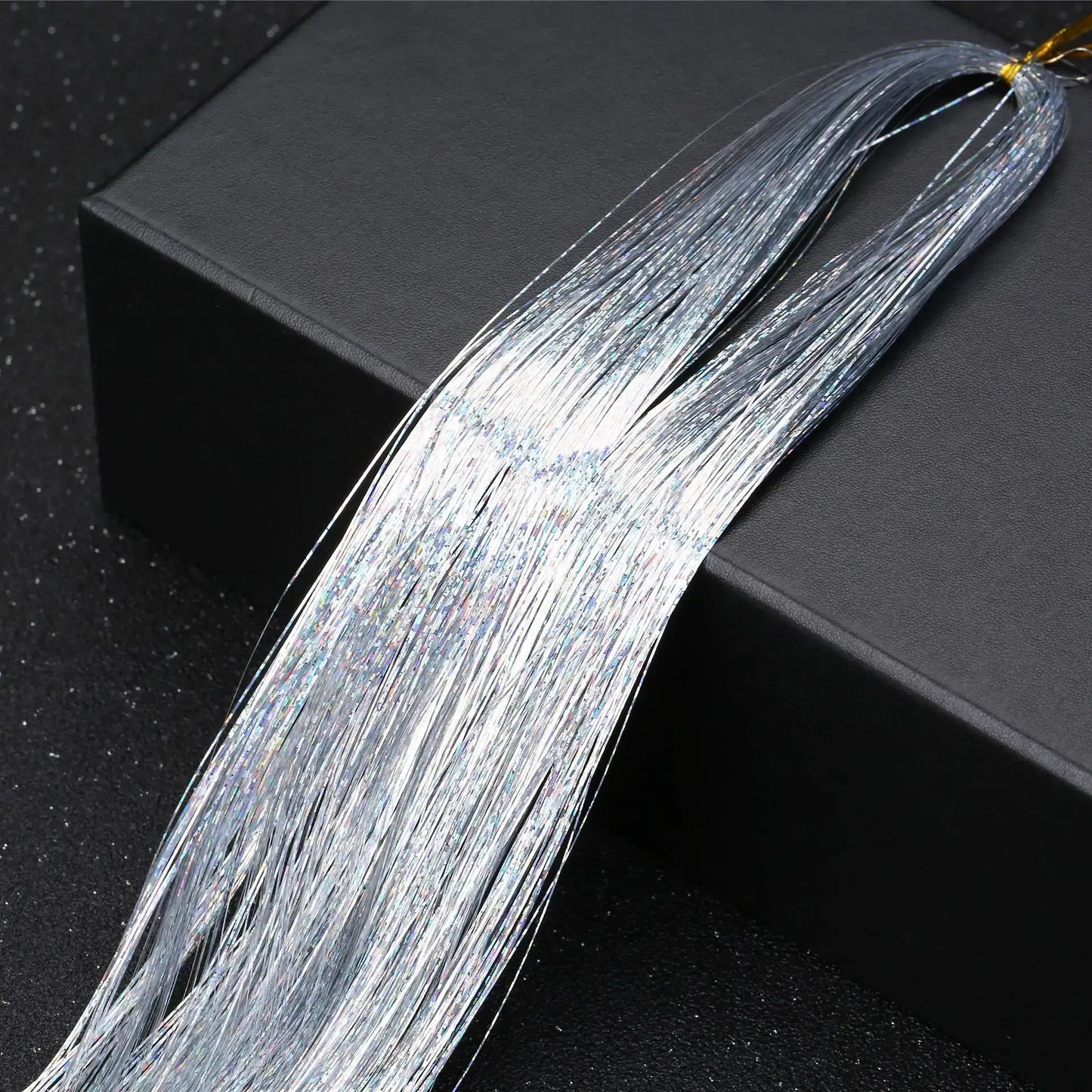 Silver glitter hair tinsel bundle atop black box, showcasing vibrant shine and texture for parties and festive hairstyles.