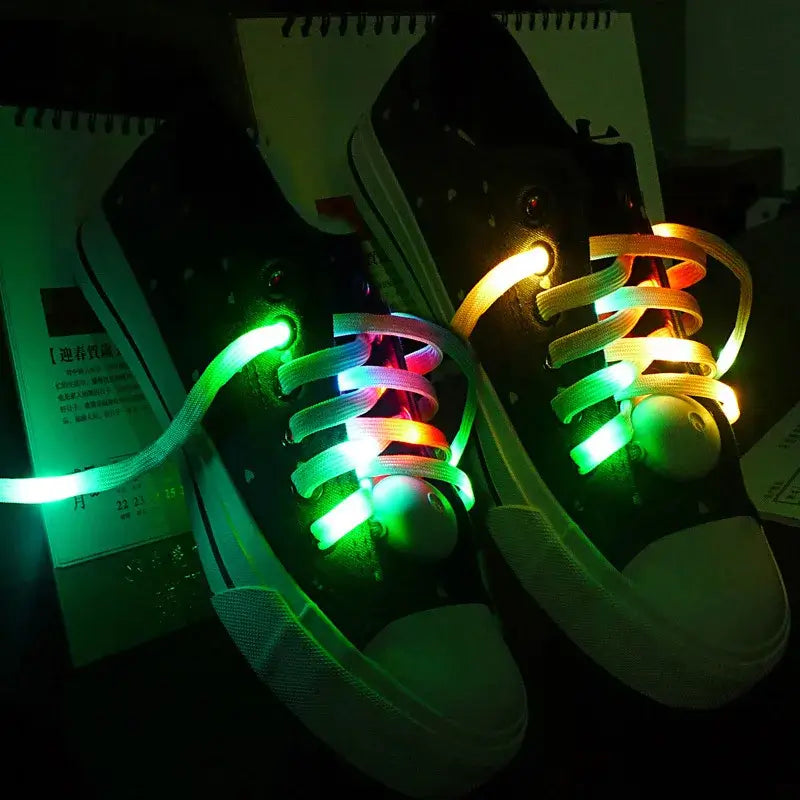 LED light-up shoelaces glowing in multiple colors on black sneakers in the dark.