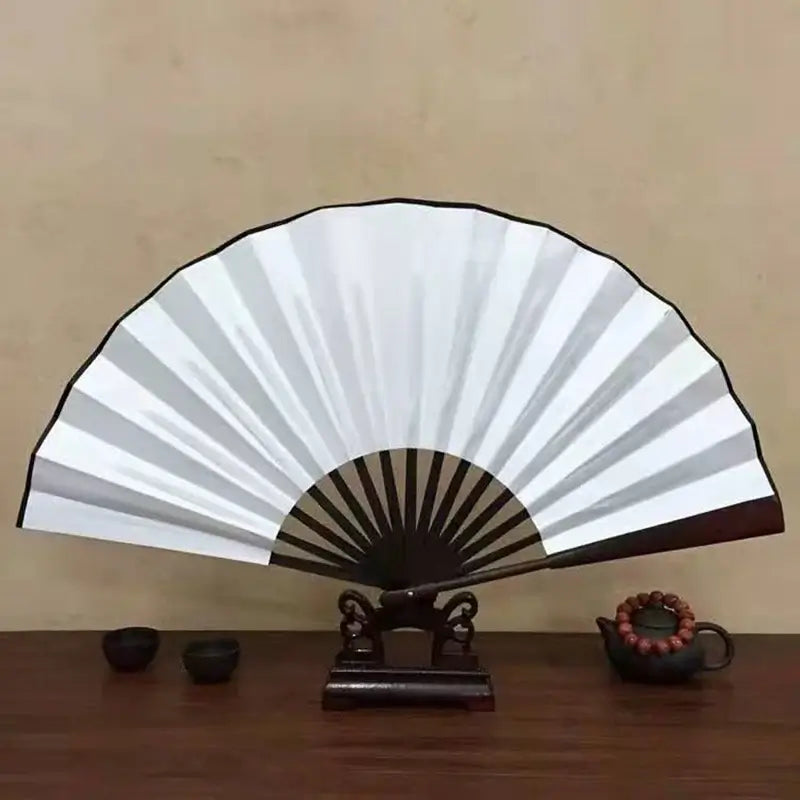 Elegant white folding fan displayed on a wooden table with decorative items.