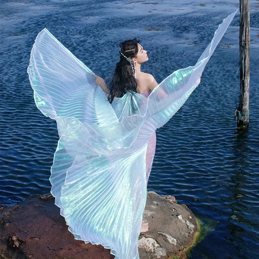 Performer wearing iridescent Isis wings on a rock by the water, showcasing grand 300-degree design for dance and festival events.