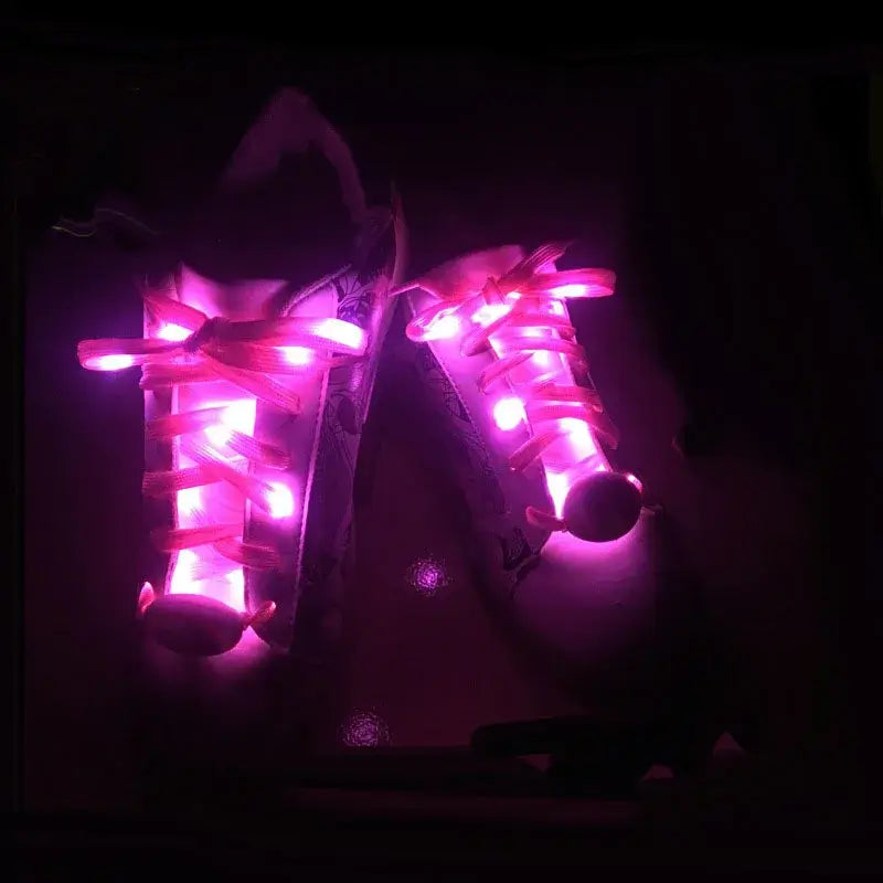 LED light-up shoelaces glowing pink on white sneakers in the dark, showcasing vibrant and eye-catching illumination.