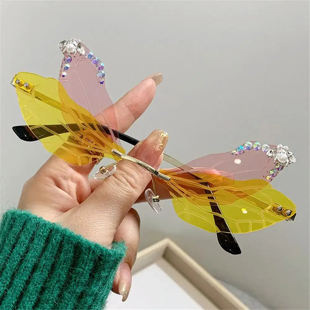 Hand holding dragonfly wings sunglasses with diamond embellishments, luxury fashion accessory for parties.