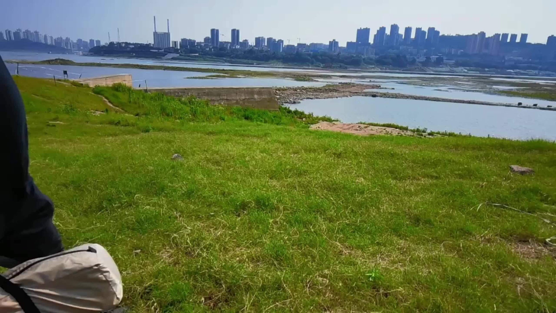 Scenic view of green grasslands with a distant city skyline and river under a clear blue sky.