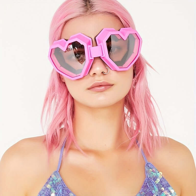 Woman wearing pink oversized heart-shaped Y2K fashion glasses with mirrored lenses at a festival.