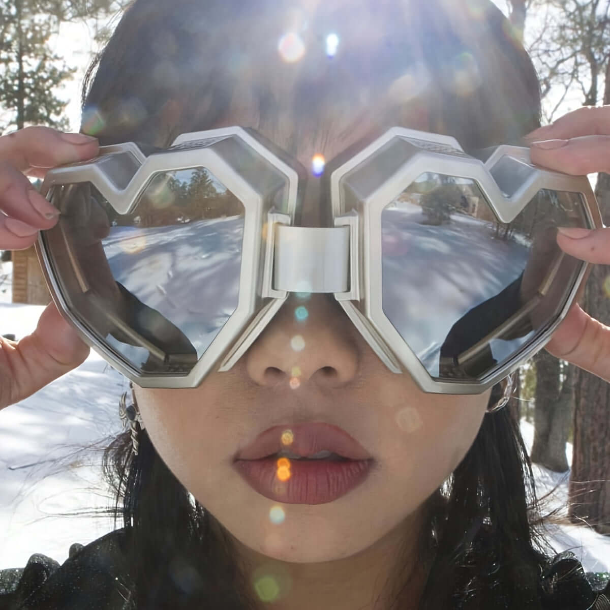 Oversized heart-shaped Y2K mirrored glasses worn outdoors with sun flare, reflecting a snowy landscape.