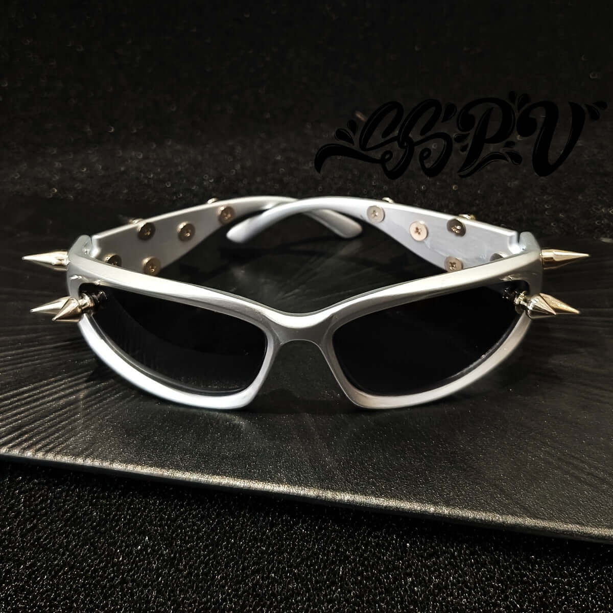 Cyberpunk cat-eye glasses with rivet accents and anti-reflective lenses on a textured surface, stylish rave fashion eyewear.