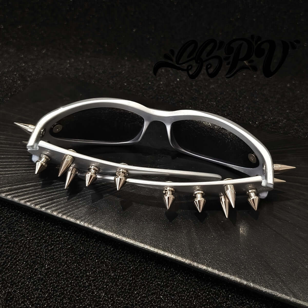 Cyberpunk cat-eye glasses with metal rivet accents on a black surface, showcasing bold fashion eyewear for raves and parties.